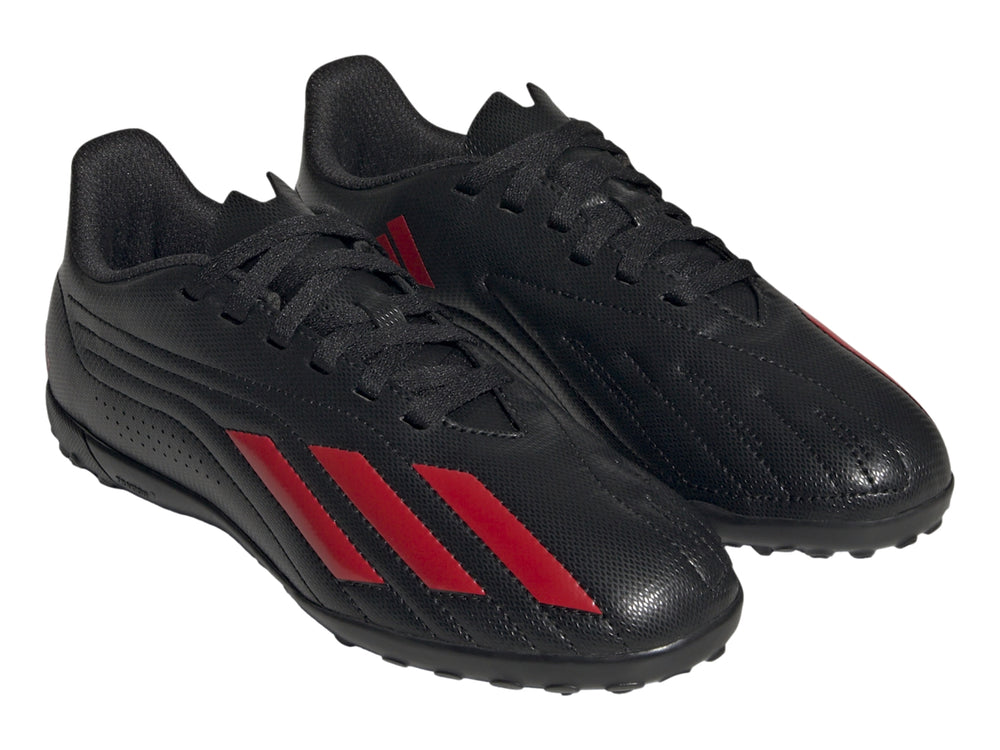 Calzado de fútbol Adidas negro con franjas rojas y suela para césped sintético.