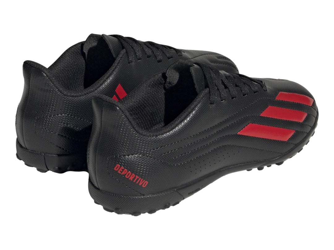 Calzado de fútbol Adidas negro con franjas rojas y suela para césped sintético.
