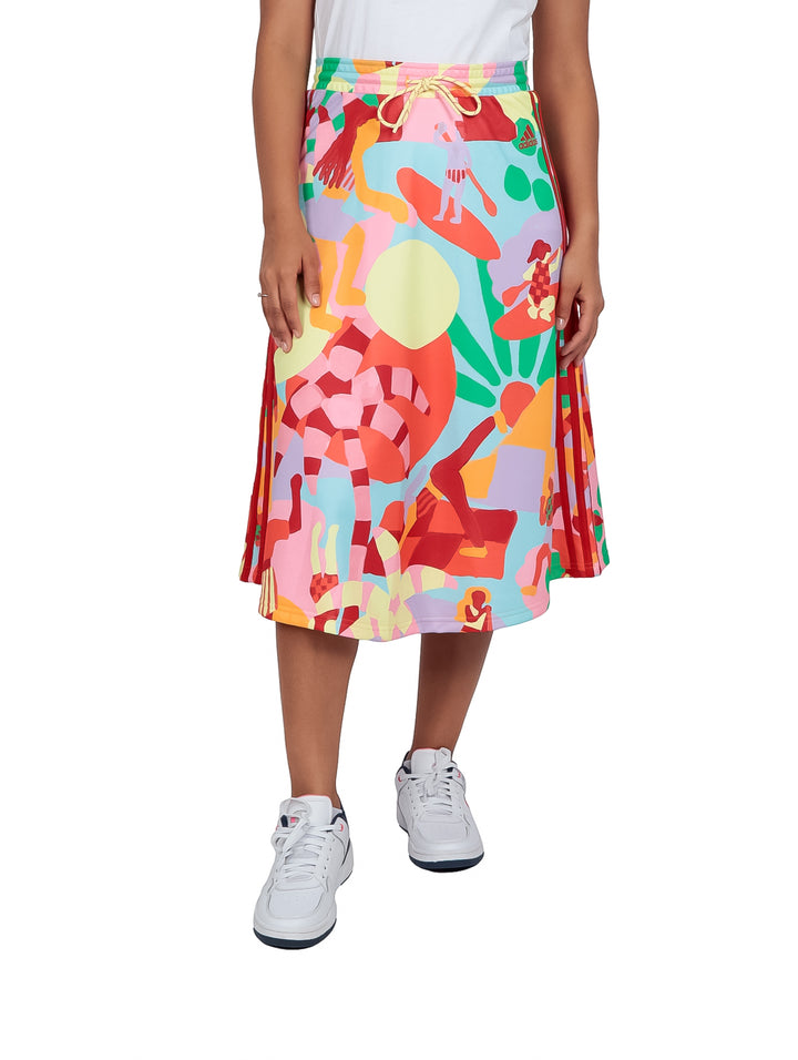 Mujer vistiendo falda deportiva Adidas multicolor con estampado abstracto y tenis blancos.