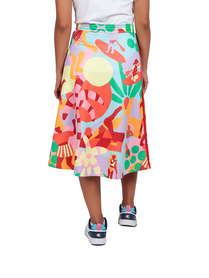 Mujer vistiendo falda deportiva Adidas multicolor con estampado abstracto y tenis blancos.