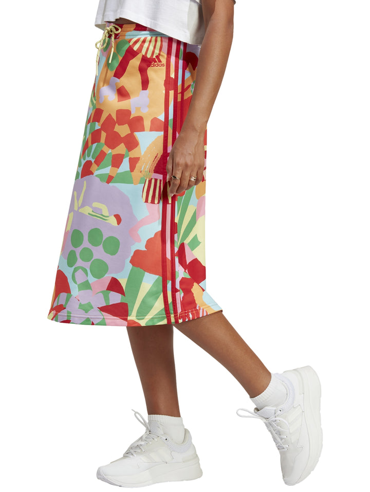 Mujer vistiendo falda deportiva Adidas multicolor con estampado abstracto y tenis blancos.