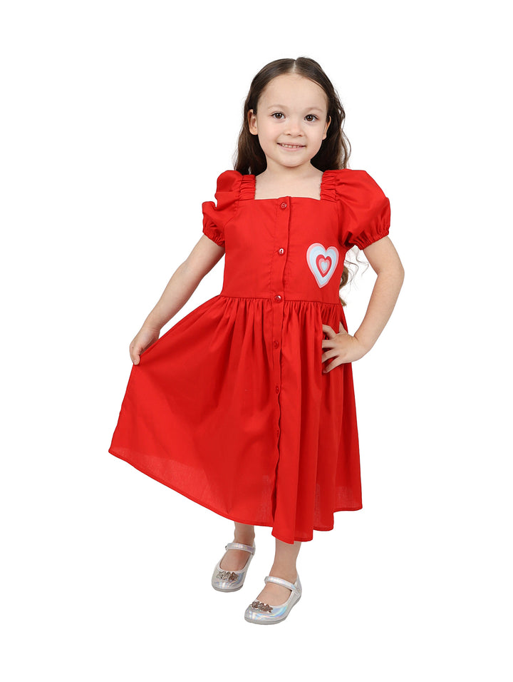 Niña vistiendo un vestido rojo de popelina con botones frontales y un detalle de corazón blanco.
