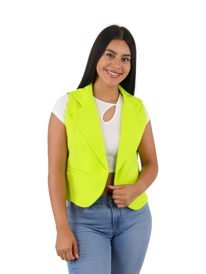 Mujer vistiendo un chaleco color lima brillante sobre una blusa blanca y jeans azules.