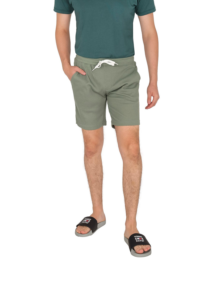 Hombre usando shorts de surf color olivo con cordón blanco.