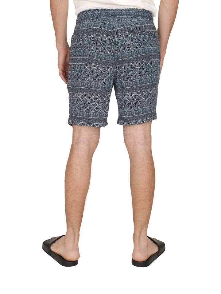 Hombre usando shorts de baño azules con estampado étnico y cordones blancos.