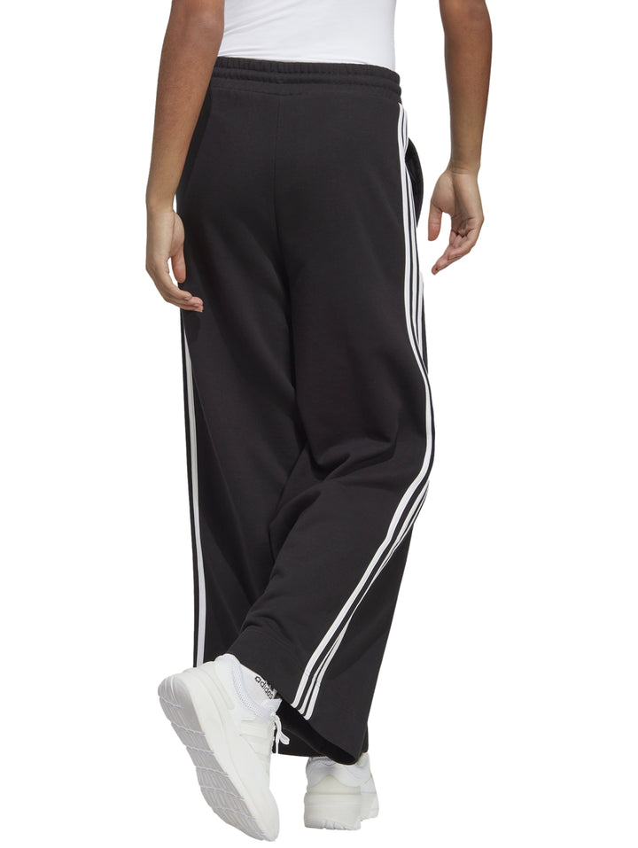 Pantalones deportivos Adidas de pierna ancha en color negro con tres franjas blancas laterales.