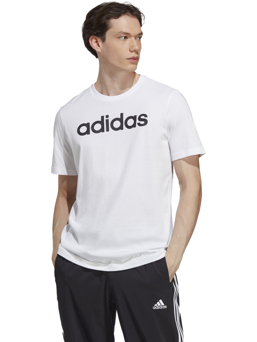 Hombre vistiendo playera blanca de manga corta con logotipo de Adidas en negro y pantalones deportivos negros.