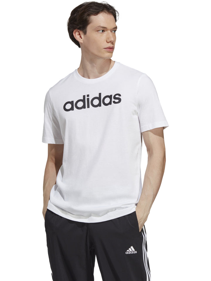 Hombre vistiendo playera blanca de manga corta con logotipo de Adidas en negro y pantalones deportivos negros.