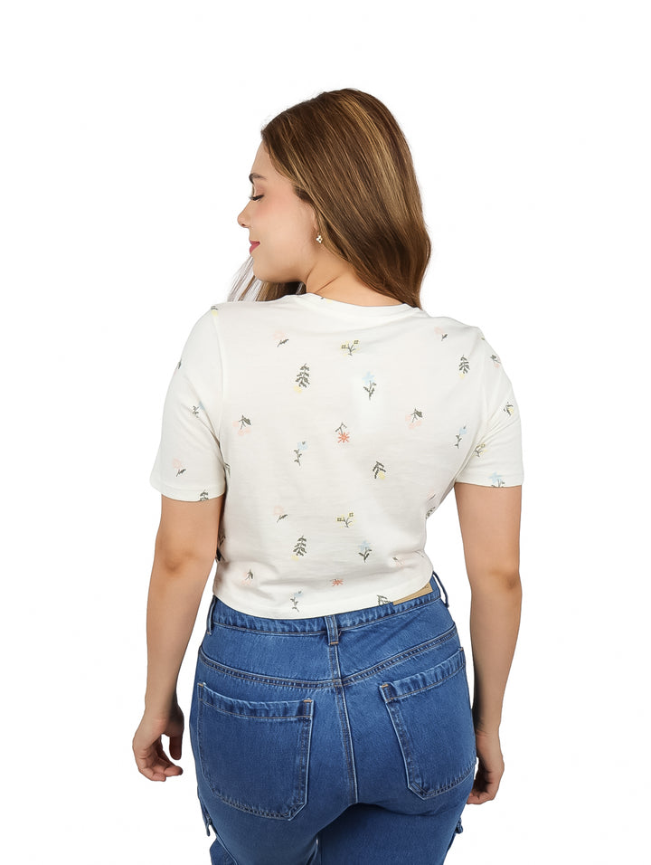 Mujer vistiendo camiseta crop blanca de VANS con estampado floral y pantalones vaqueros.