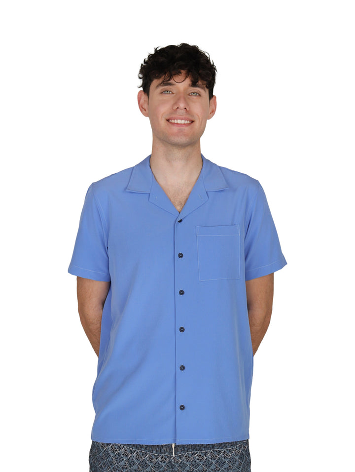 Hombre vistiendo una camisa casual de manga corta en color azul con cuello abierto y un bolsillo en el pecho.
