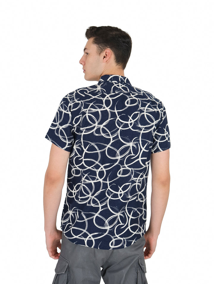 Hombre vistiendo camisa de manga corta azul marino con estampado de círculos blancos y pantalones grises.