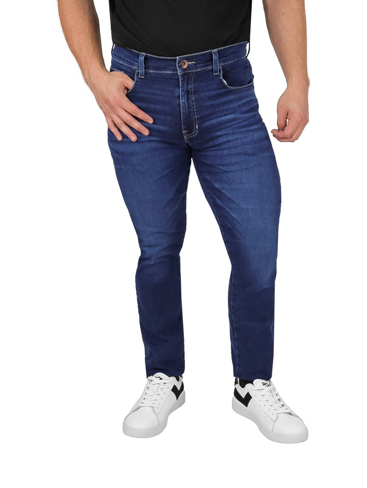 Hombre vistiendo pantalones jeans OGGI color azul oscuro Dark Stone y tenis blancos.