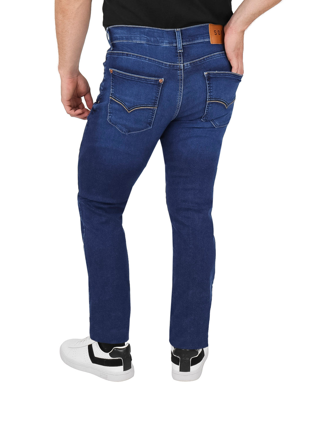 Hombre vistiendo pantalones jeans OGGI color azul oscuro Dark Stone y tenis blancos.