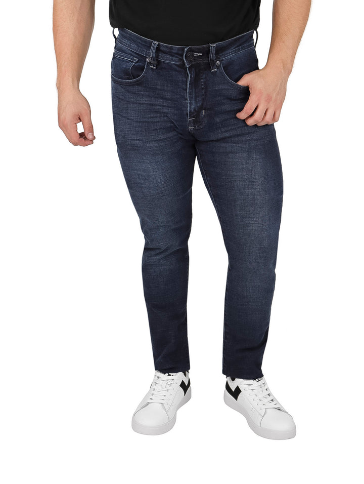 Hombre vistiendo pantalones jeans de color azul oscuro y tenis blancos sobre fondo blanco.