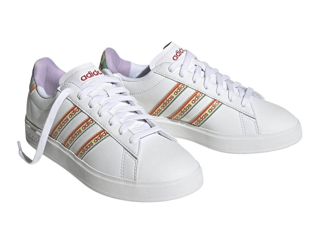 Tenis Adidas blancos con franjas laterales multicolor y suela blanca.
