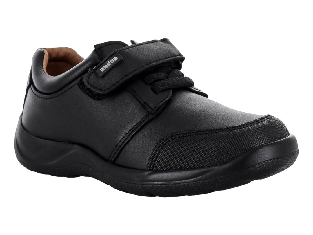 Zapato casual negro para niño con cierre de velcro y cordones sobre fondo blanco.