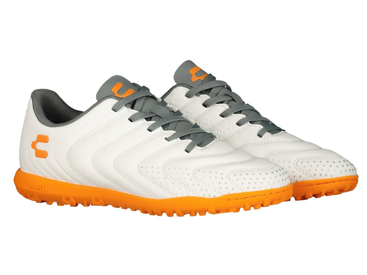 Par de zapatos de fútbol Charly color blanco con suela y detalles en naranja y agujetas grises.