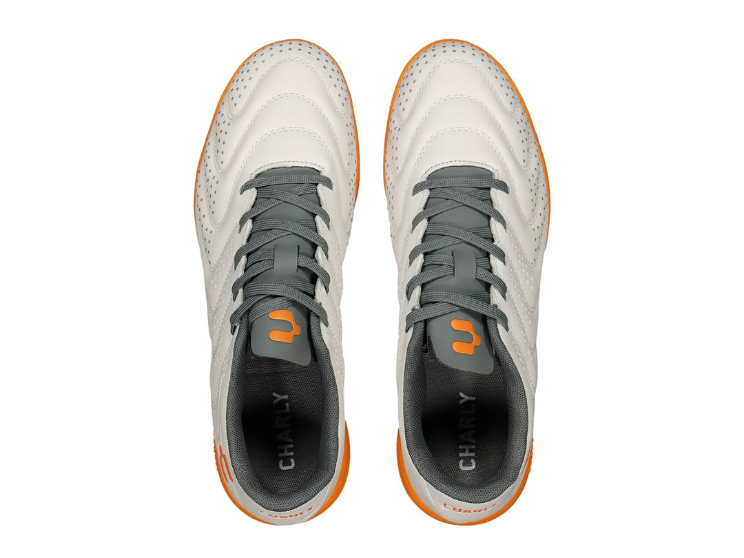 Par de zapatos de fútbol Charly color blanco con suela y detalles en naranja y agujetas grises.