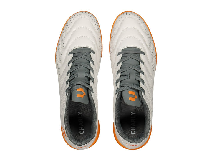 Par de zapatos de fútbol Charly color blanco con suela y detalles en naranja y agujetas grises.