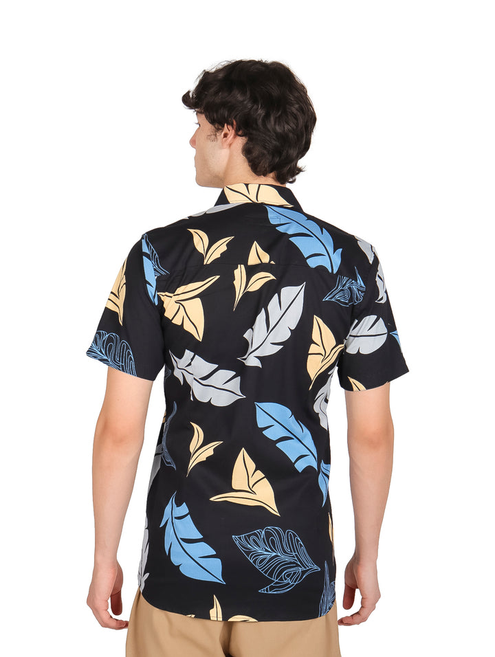 Hombre vistiendo camisa negra de manga corta con estampado de hojas en colores azul y amarillo.