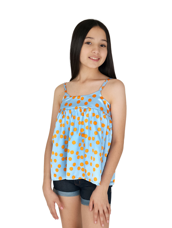 Niña vistiendo blusa de seda color cielo con lunares naranjas.