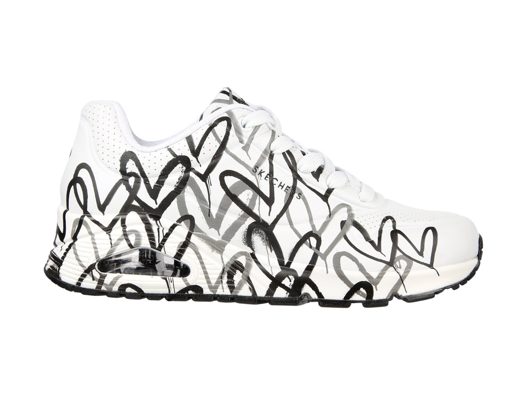 Tenis Skechers blancos con estampado de corazones en negro y gris, diseño deportivo con suela blanca y negra.