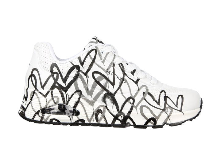 Tenis Skechers blancos con estampado de corazones en negro y gris, diseño deportivo con suela blanca y negra.