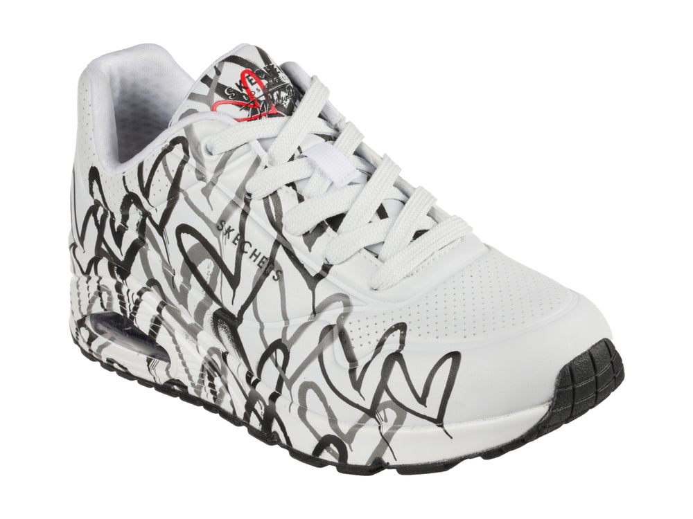 Tenis Skechers blancos con estampado de corazones en negro y gris, diseño deportivo con suela blanca y negra.