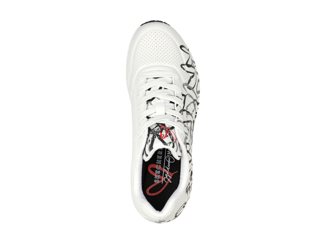 Tenis Skechers blancos con estampado de corazones en negro y gris, diseño deportivo con suela blanca y negra.