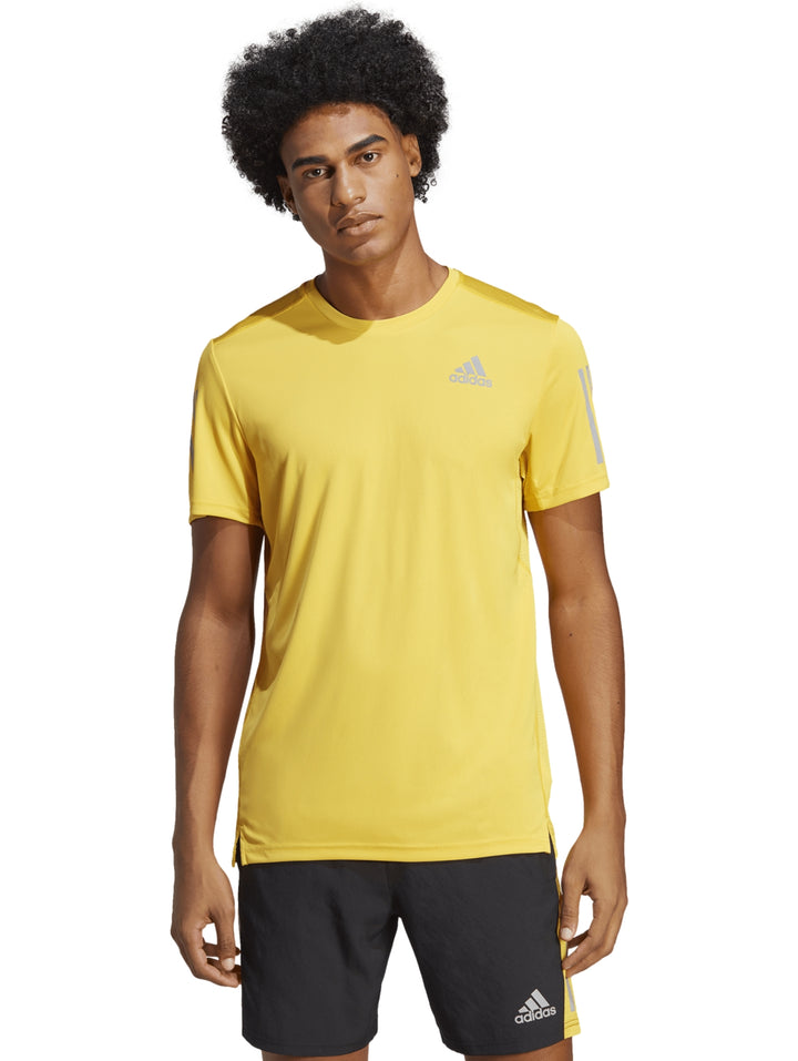 Hombre usando camiseta Adidas Own The Run color amarillo y shorts negros.