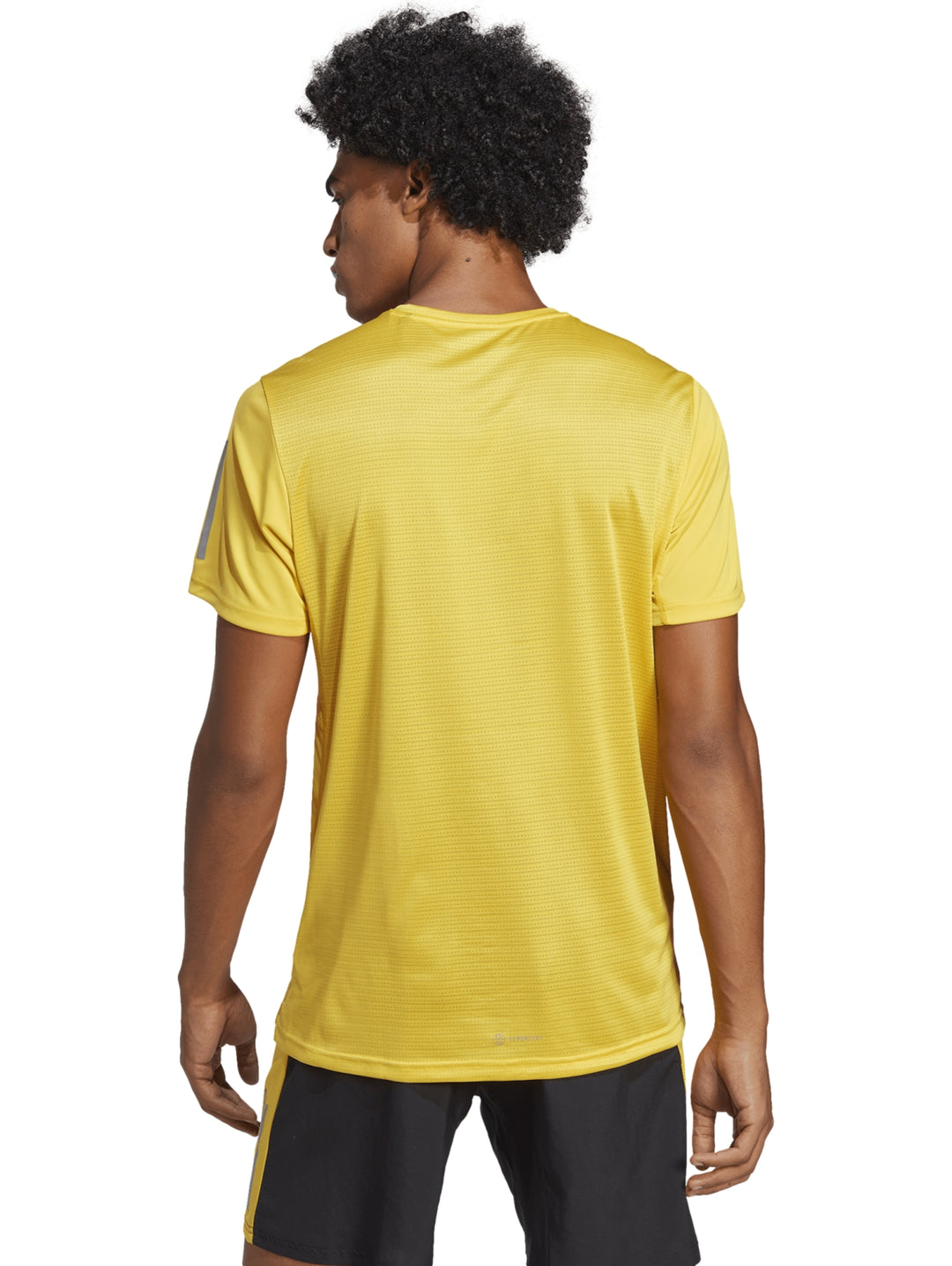 Hombre usando camiseta Adidas Own The Run color amarillo y shorts negros.