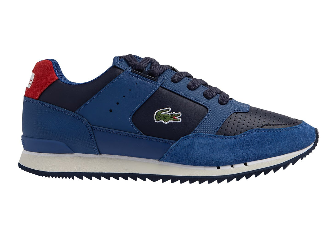Tenis deportivos Lacoste en tonos azul y azul marino con suela blanca y detalle rojo en el talón.