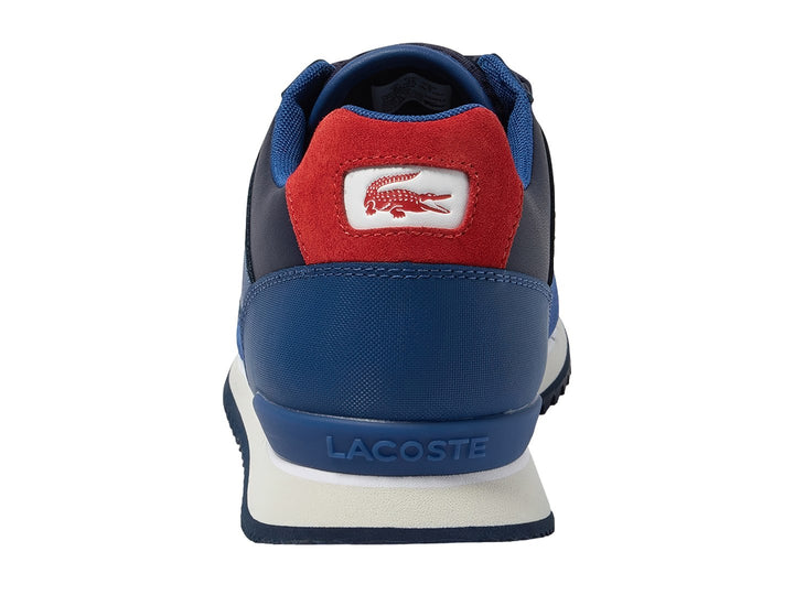 Tenis deportivos Lacoste en tonos azul y azul marino con suela blanca y detalle rojo en el talón.