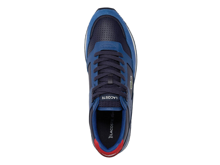 Tenis deportivos Lacoste en tonos azul y azul marino con suela blanca y detalle rojo en el talón.
