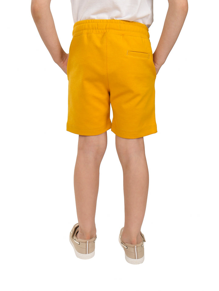 Niño vistiendo shorts color mostaza con cordón ajustable en la cintura.
