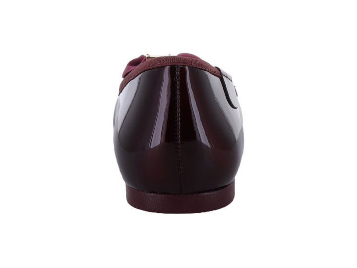 Zapatos planos color wine con acabado brillante, decorados con un moño y herraje dorado en la punta.