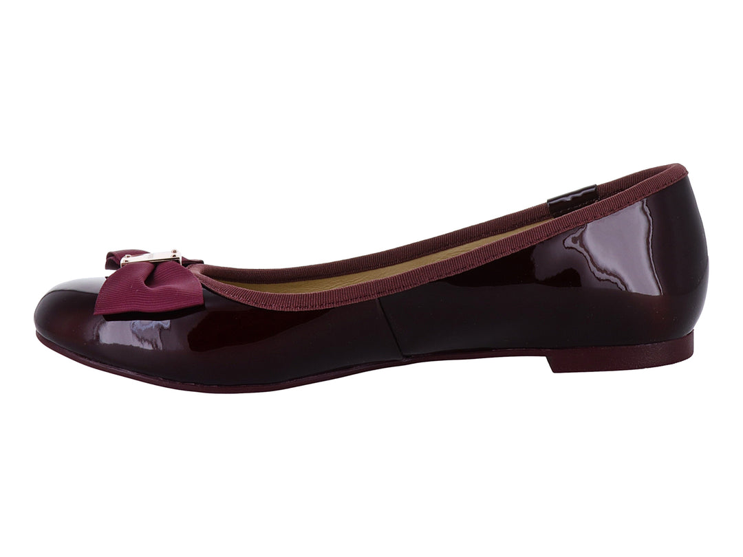 Zapatos planos color wine con acabado brillante, decorados con un moño y herraje dorado en la punta.