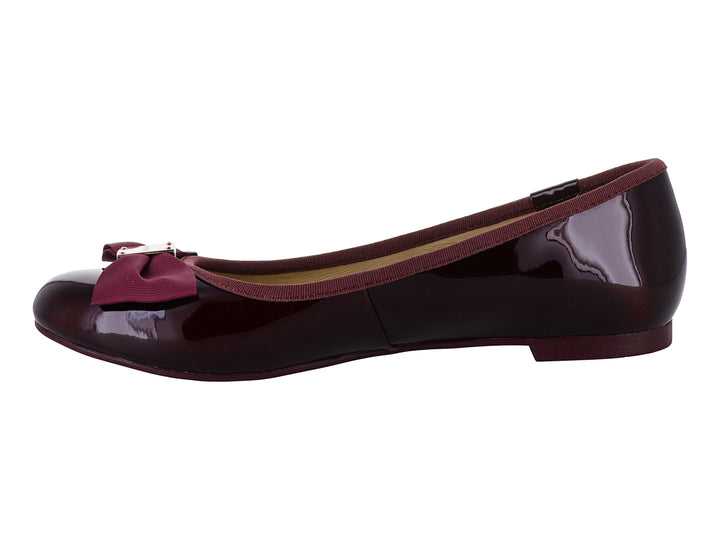Zapatos planos color wine con acabado brillante, decorados con un moño y herraje dorado en la punta.