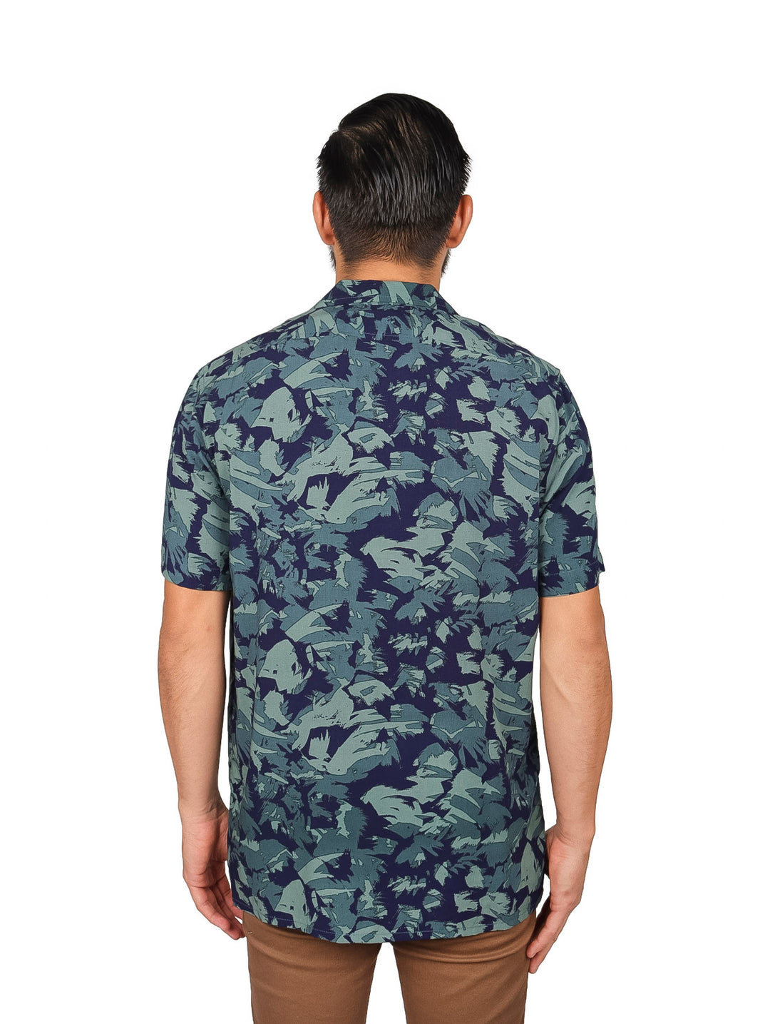 Hombre vistiendo camisa de manga corta con estampado floral en tonos verde y azul marino.