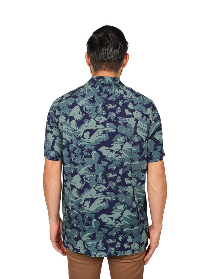 Hombre vistiendo camisa de manga corta con estampado floral en tonos verde y azul marino.