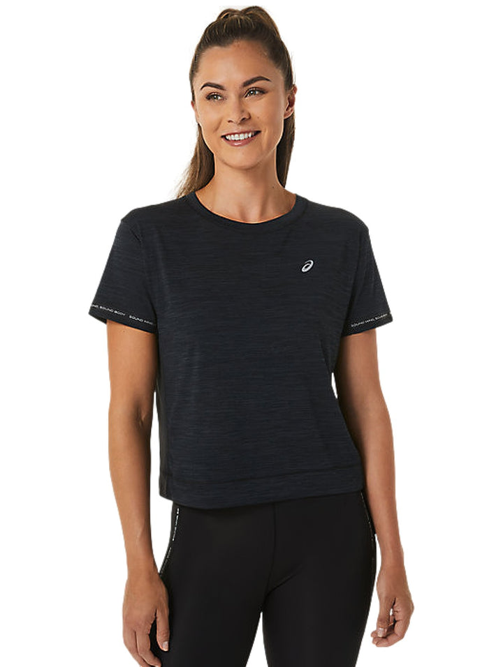 Mujer vistiendo un crop top deportivo ASICS color negro carbón y leggings negros.