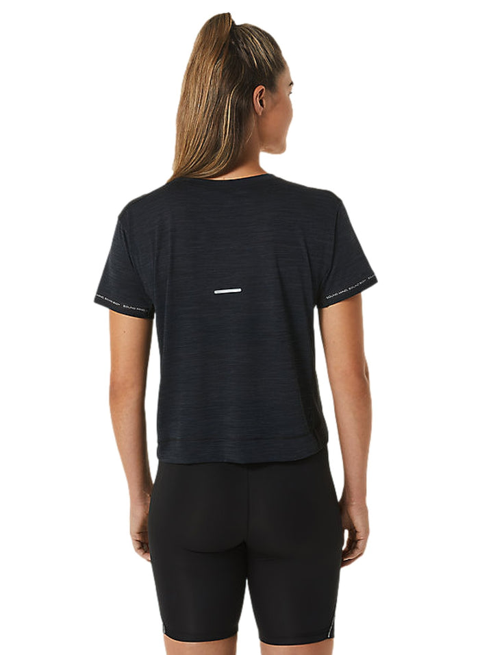 Mujer vistiendo un crop top deportivo ASICS color negro carbón y leggings negros.