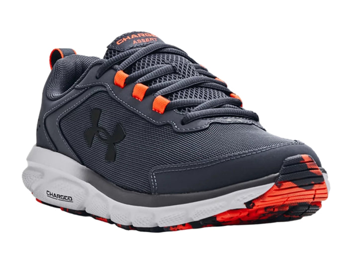 Tenis deportivos Under Armour color gris con suela blanca y detalles en naranja.