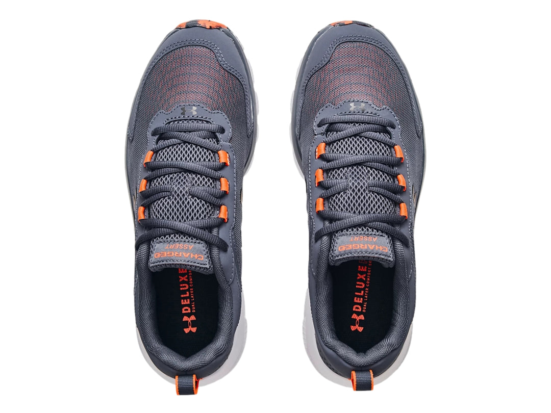 Tenis deportivos Under Armour color gris con suela blanca y detalles en naranja.