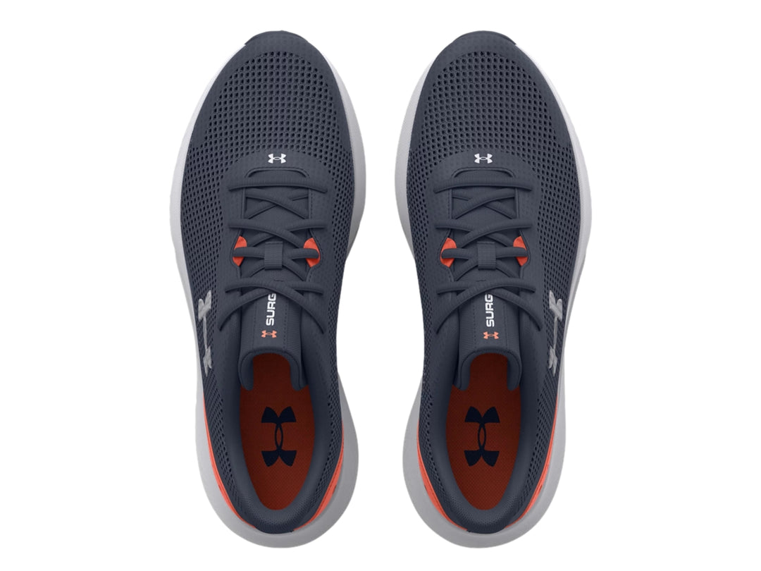 Tenis deportivos Under Armour color gris con suela blanca y detalle naranja en el talón.