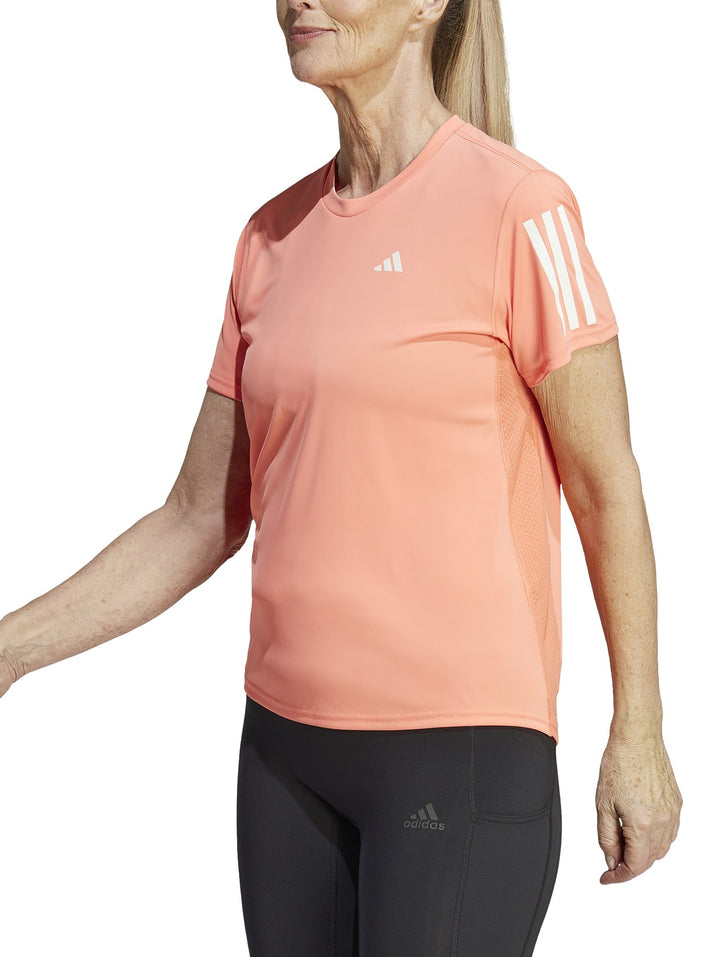 Camiseta deportiva Adidas color coral para mujer con tres franjas blancas en la manga y logo frontal blanco.