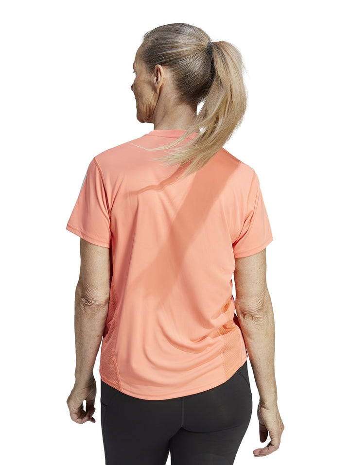 Camiseta deportiva Adidas color coral para mujer con tres franjas blancas en la manga y logo frontal blanco.