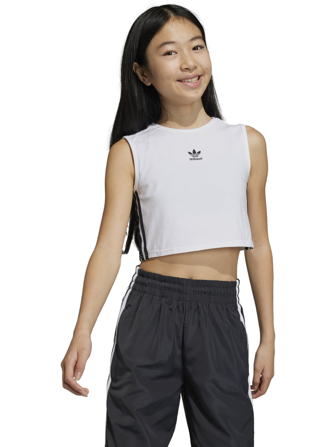 Niña usando un crop tank top blanco de Adidas con rayas negras laterales y pantalones deportivos oscuros.