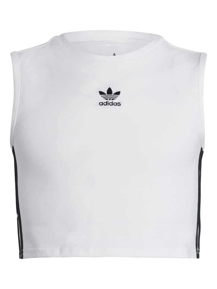 Niña usando un crop tank top blanco de Adidas con rayas negras laterales y pantalones deportivos oscuros.