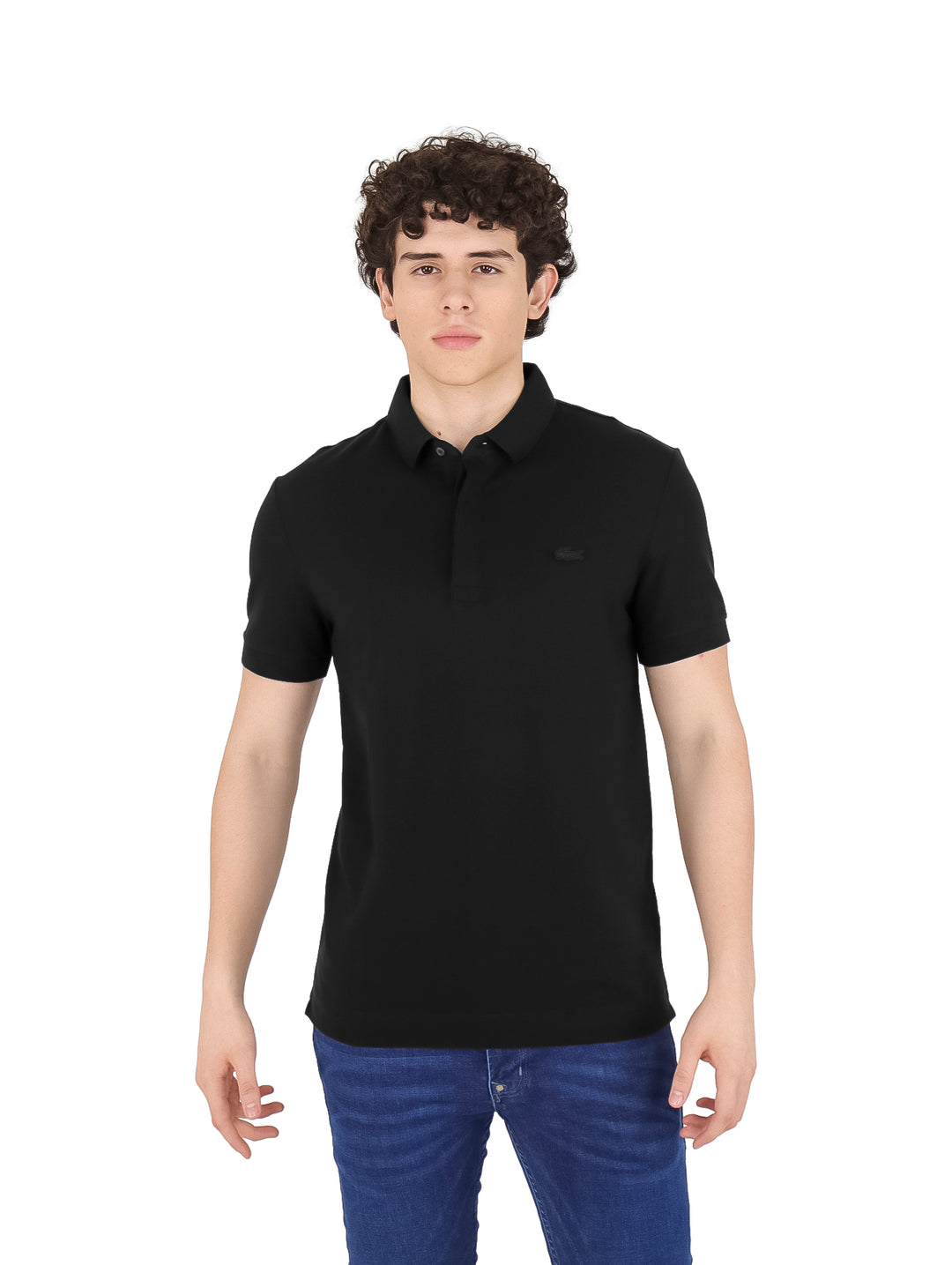 Hombre vistiendo una playera polo Lacoste de color negro y pantalones vaqueros azules.